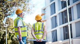 Two electricians in safety gear looking up at a corporate building